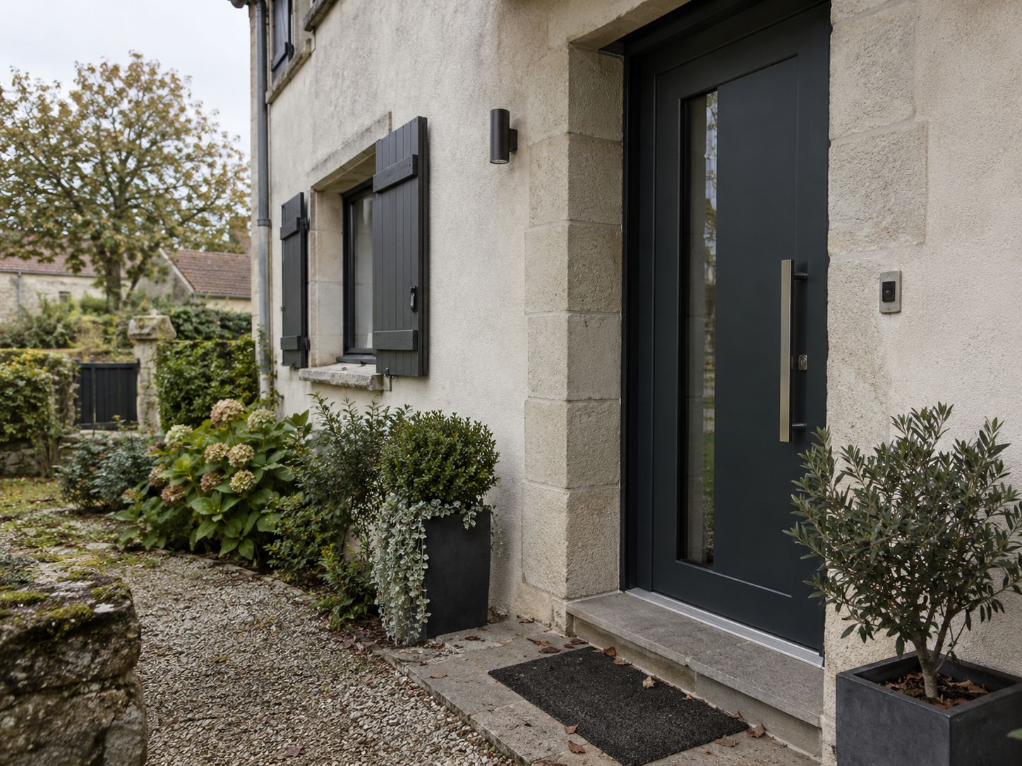Porte d’entrée aluminium anthracite avec poignée bâton, posée sur une maison en pierre.