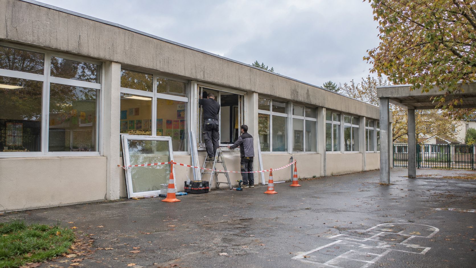Remplacement de fenêtres sur un bâtiment scolaire, zone de travaux balisée dans la cour.